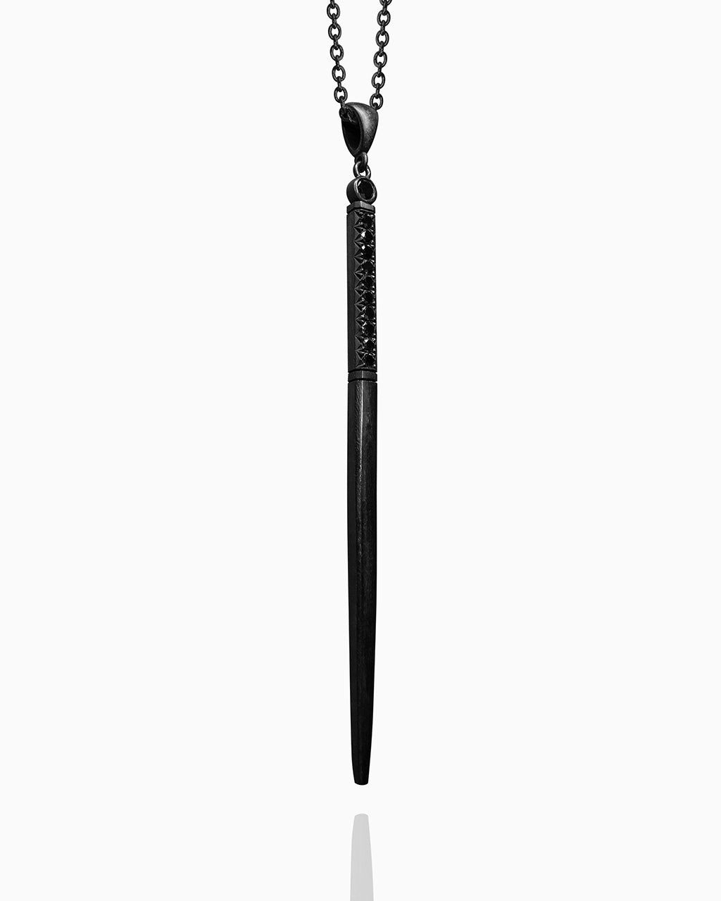 A blackened wand necklace made from sterling silver hanging on a blackened chain against a white background. The handle at the top of the wand is set with a single row of black diamonds, with a larger black diamond set in a round bezel at the very top. Below, there are two carved lines and then a smooth, tapered square shaft.